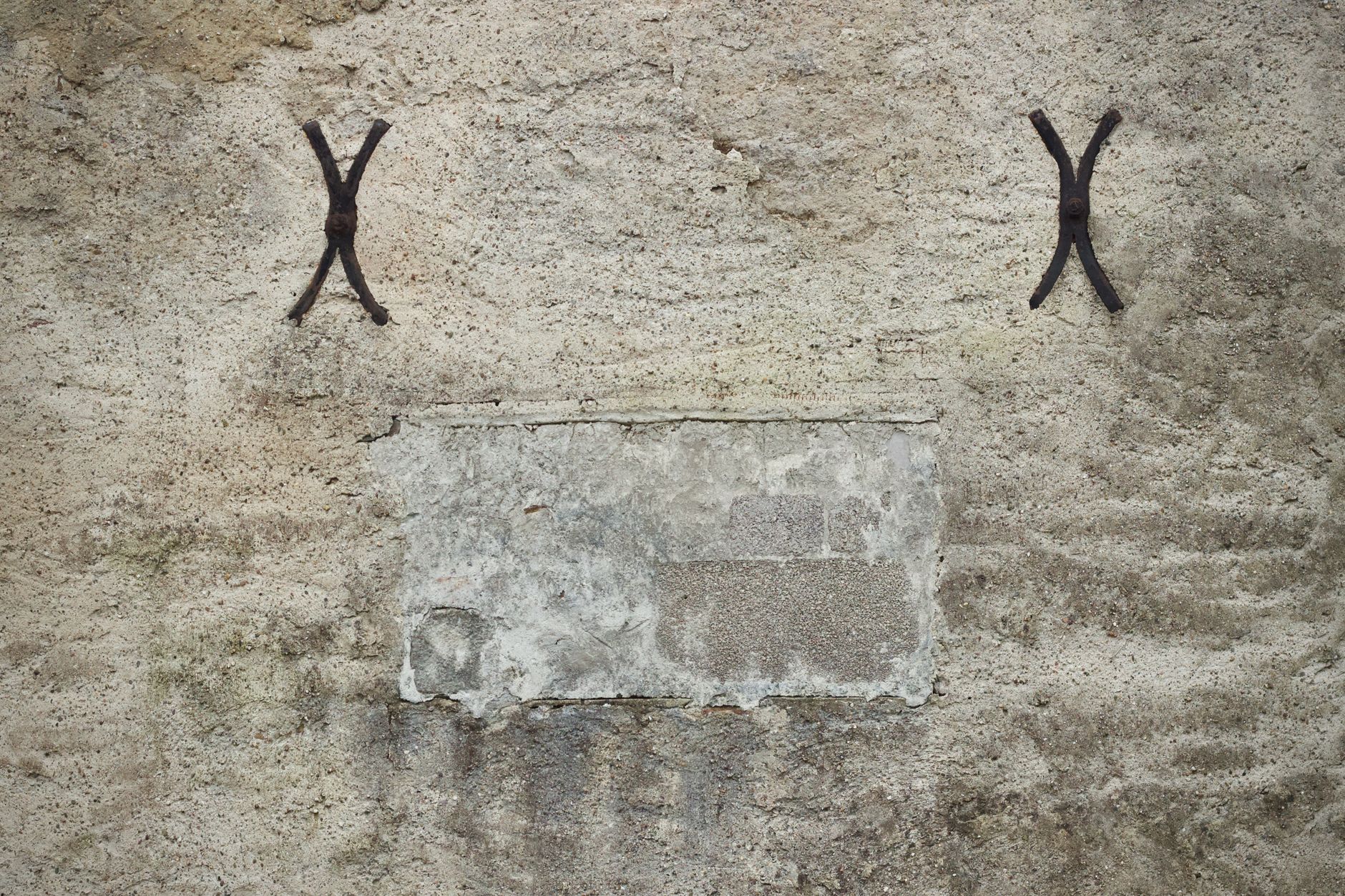 Close-up of a textured stone wall featuring old iron brackets and weathered patches.