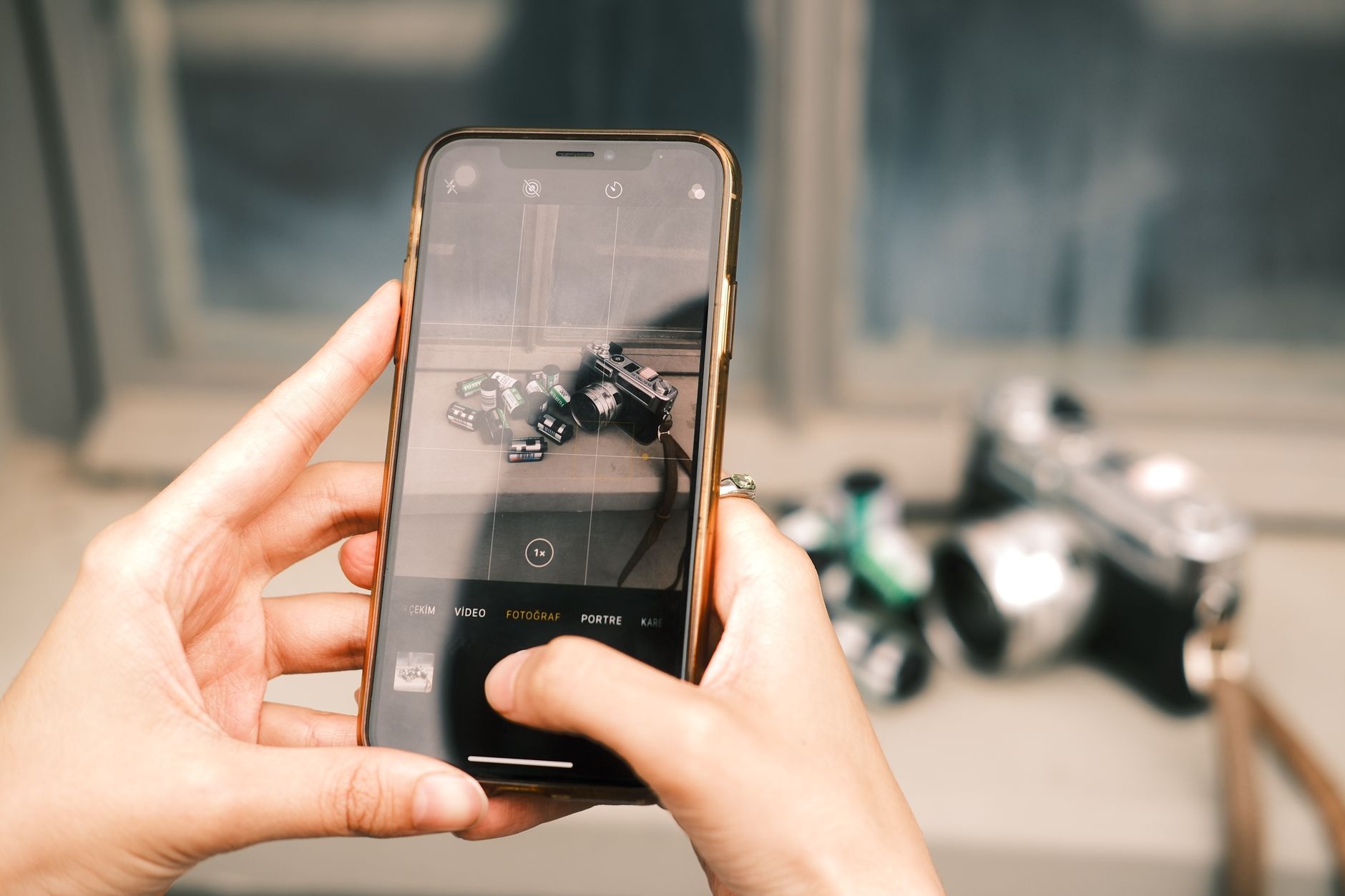 A close-up shot of hands using a smartphone to photograph vintage cameras.