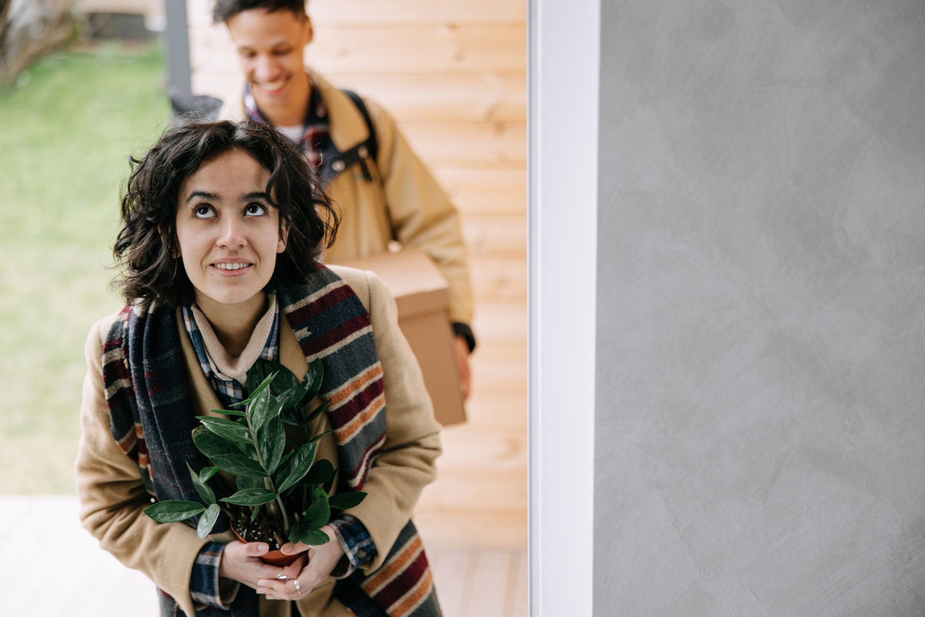 A cheerful couple moving into their new home, carrying a potted plant and a box, symbolizing new beginnings.